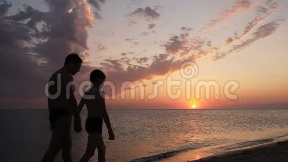 日落时分父子俩在海滩上散步友好家庭观念视频的预览图