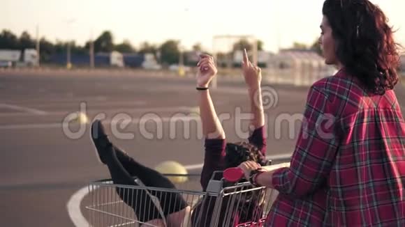 一个年轻女子推着一辆购物车和她的女朋友在商场的停车场里视频的预览图
