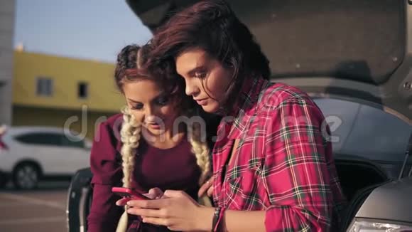 两个年轻漂亮的女朋友看着智能手机坐在里面看照片的特写镜头视频的预览图