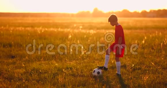 日落时分一名男孩足球运动员在球场上抛球视频的预览图