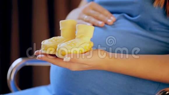 怀孕的快乐女人手里拿着婴儿鞋妈妈在等她的孩子孕妇肚皮怀孕生育观念视频的预览图