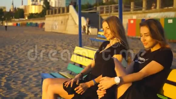 两个年轻女子坐在长凳上欣赏日落摆姿势视频的预览图