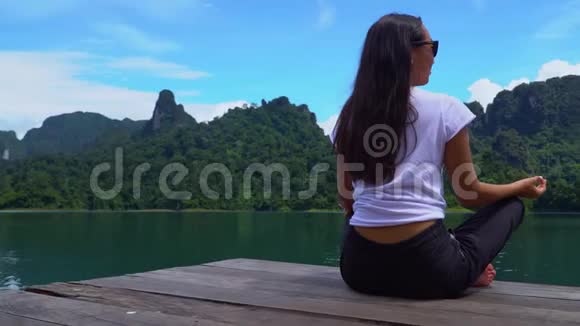 亚洲女孩坐在码头上在一个湖上摆着一个莲花姿势景色很美视频的预览图