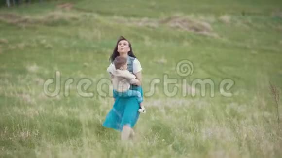 妈妈抱着宝宝和他一起旋转夏天走在田野上阴天视频的预览图