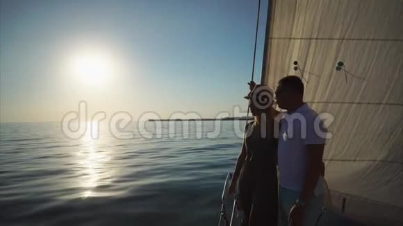 年轻男子和他一起优雅的女朋友正站在游艇边上扬起风帆视频的预览图