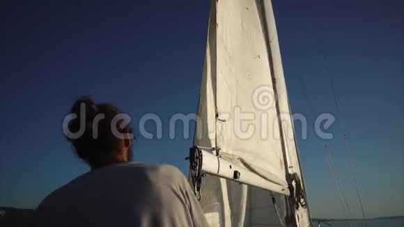 在阳光明媚的日子里黑发男子正在帆船上批改巨大的帆视频的预览图
