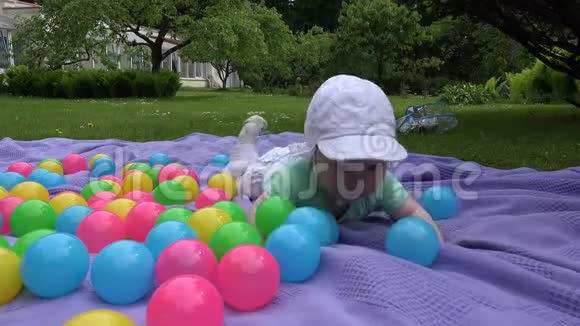可爱的女婴戴着白帽子在格子布上五颜六色的球间爬行4K视频的预览图
