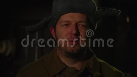 俄罗斯男人戴着一顶带耳罩的帽子在黑暗的地下室里打电话决定国家大事视频的预览图