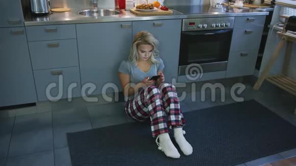 可爱的女人在厨房地板上浏览智能手机视频的预览图