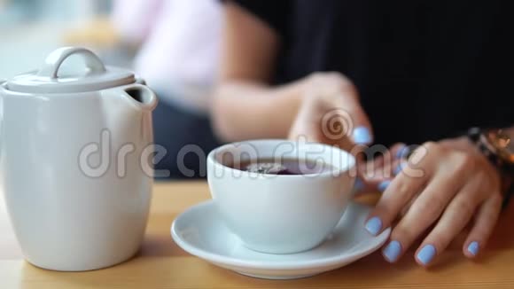 从木桌上拿着一个带热茶的白色杯子的女性手的特写然后相机用杯子向上移动视频的预览图