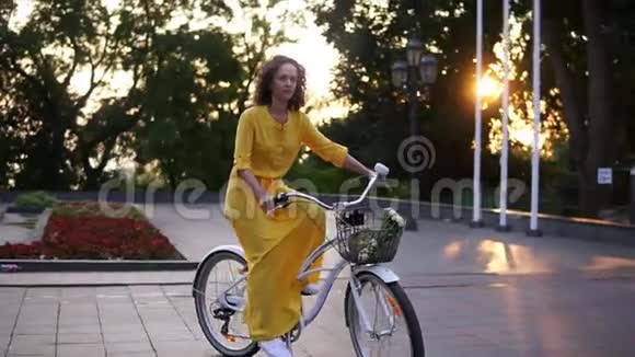 年轻迷人的女人骑着一辆城市自行车在太阳升起的时候城市公园里有一个篮子和花贷款视频的预览图