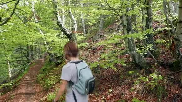 女背包客在森林内的步道上徒步旅行观看电影视频的预览图