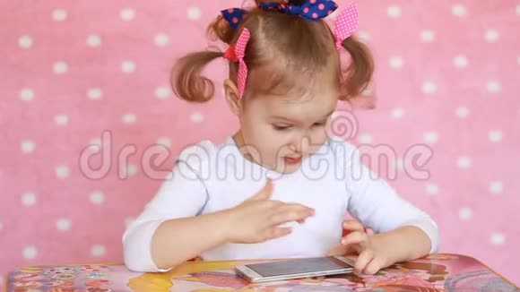 孩子玩手机一个漂亮的小女孩用智能手机玩游戏视频的预览图