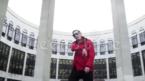 穿着红色运动服和太阳镜的有魅力的男性在花岗岩柱旁边唱歌视频的预览图
