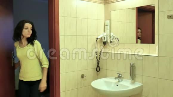 在浴室的洗脸盆里一个穿着黄色衬衫和深色头发洗手的年轻女孩的后景肖像视频的预览图