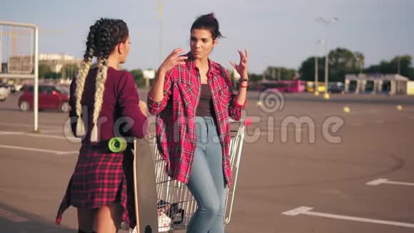 日落时分两个年轻的女人站在购物车旁停着车穿格子衬衫的女孩视频的预览图