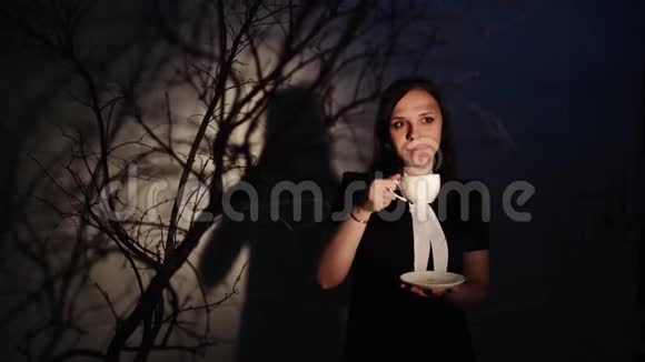 女人在黑暗的地方喝咖啡年轻的梦幻女子一边喝咖啡一边站在光线下视频的预览图