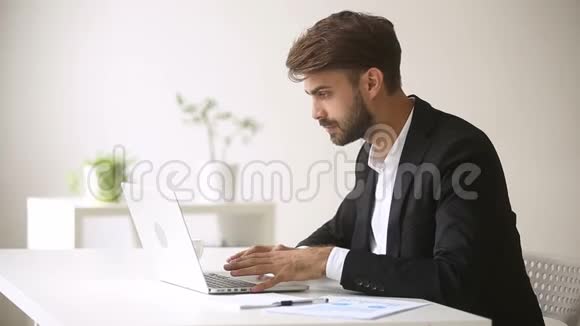 快乐的商人看着笔记本电脑笑着被网上赢兴奋视频的预览图