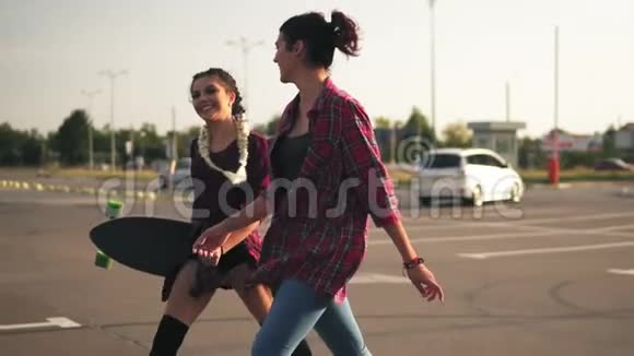 侧面看两个年轻快乐的时髦女孩一起在停车场散步谈笑风生一个长得很长的女孩视频的预览图