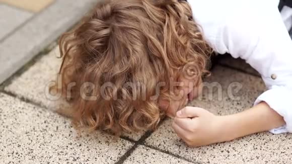 卷发男学生玩得很开心那男孩跌倒在柏油路上拳头打在铺路石上视频的预览图