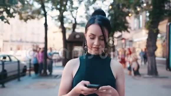 美丽的年轻女孩使用她的手机而走在城市的街道上抚摸她的头发短信微笑存在于视频的预览图
