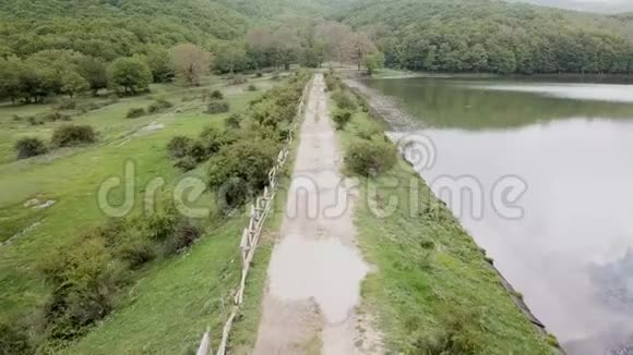 无人驾驶飞机在一条沿着湖泊行驶的乡村道路上飞行视频的预览图