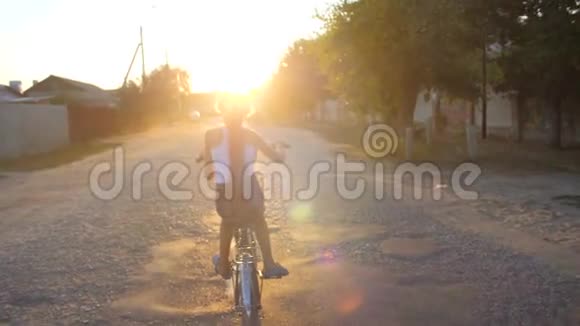 女孩骑着自行车在夕阳的照耀下沿着道路行驶慢动作视频的预览图