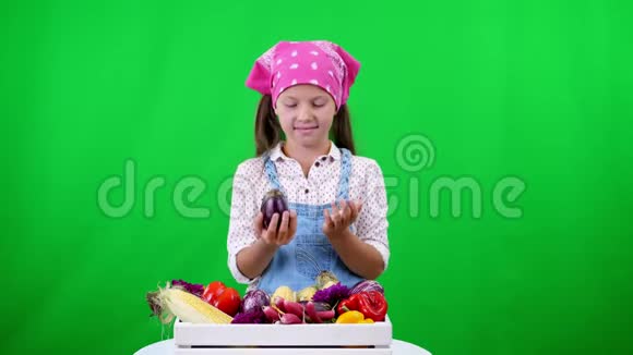 可爱微笑小农家姑娘出示一盒不同新鲜蔬菜收获在工作室的绿色背景上视频的预览图