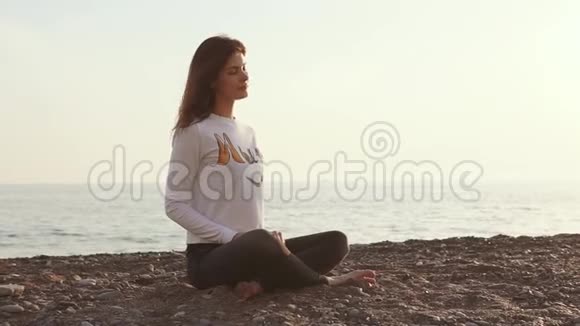 早晨女人坐在海边的鹅卵石沙滩上沉思视频的预览图