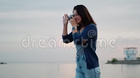 年轻女子在海边的老式相机上拍照一个有复古相机的女孩的肖像视频的预览图