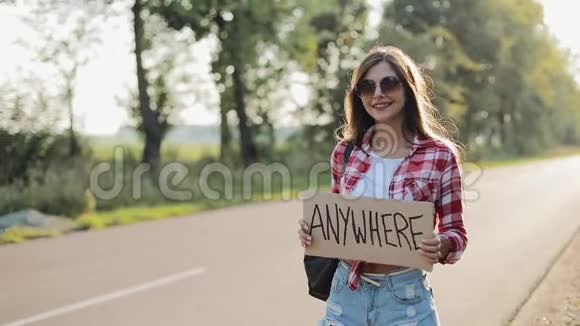 年轻漂亮的女人搭便车站在路上举着任何标志夏季视频的预览图