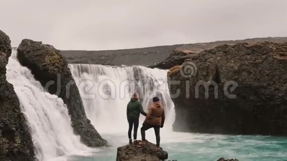 自由徒步旅行后幸福的一对夫妇站在冰岛瀑布附近一起举手视频的预览图