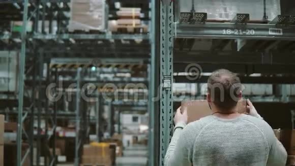 一个人正在从货架上拿箱子把它们拿走然后穿过仓库里的货架后景4K视频的预览图