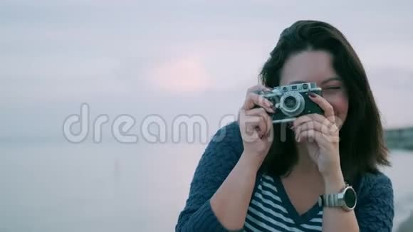 一个带复古相机的女孩的肖像年轻女子在海边的老式照相机上拍照视频的预览图