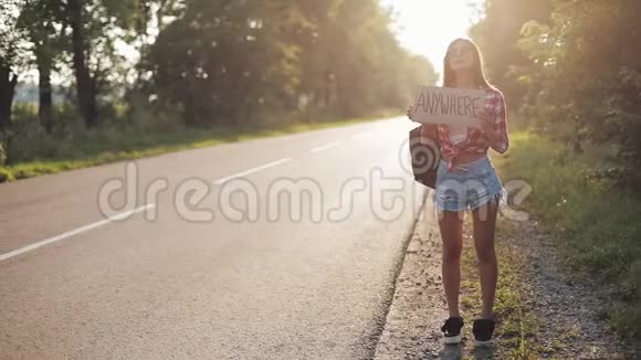 年轻漂亮的女人搭便车站在路上举着任何标志夏季视频的预览图