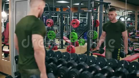 英俊健康运动的男人在镜子前的健身房里做哑铃卷曲运动4K射击视频的预览图