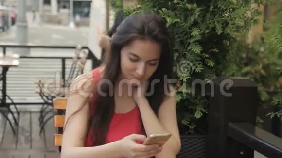 有电话的年轻女子坐在户外的夏季咖啡馆里视频的预览图