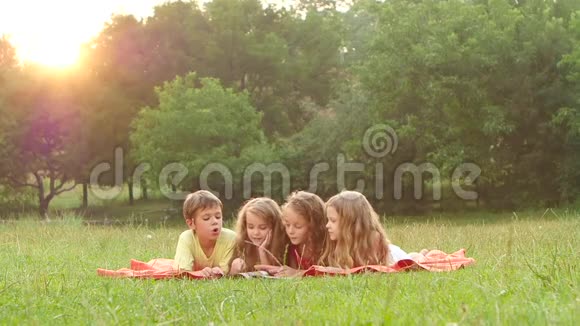 一个夏天快乐的孩子们在花园里的草坪上翻阅一本书慢动作视频的预览图