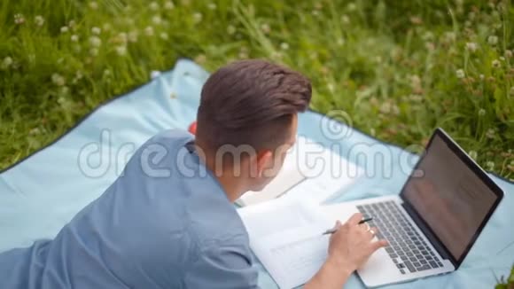 5年轻的帅哥正在玩手提电脑夏天躺在公园里视频的预览图