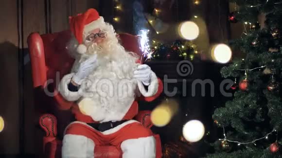 圣诞老人高兴地坐在圣诞树前的椅子上视频的预览图