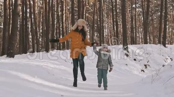 快乐的母亲和女儿在冬季森林中笑着跳着慢动作视频的预览图