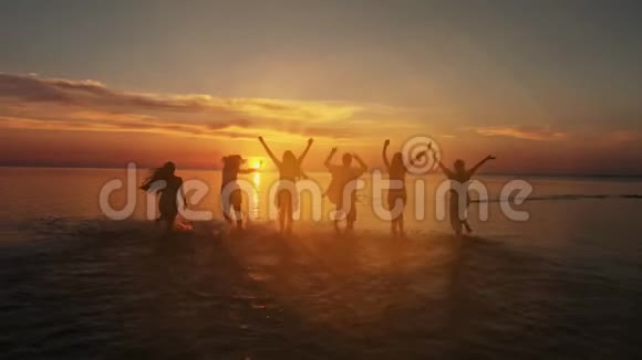 在日落时分一群快乐的朋友在水中奔跑活跃的人们在海滩上度假的剪影视频的预览图