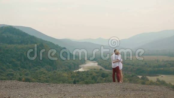 这对幸福的拥抱相爱的夫妇站在群山的边缘完整的视角无人视野视频的预览图