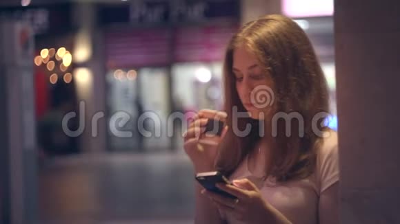 一个女孩带着咖啡和智能手机在夜城的肖像视频的预览图
