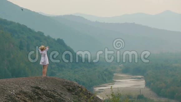 坐在美丽的金发旅行者的直升机上站在山边欣赏风景视频的预览图