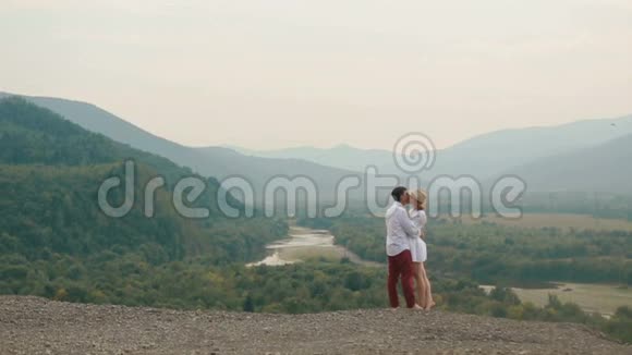 有爱的一对游客在山的边缘站在山的背景下拥抱和亲吻视频的预览图