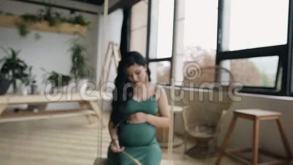 年轻漂亮的怀孕女孩长发和漂亮的耳环摆动在一个木臂和看相机视频的预览图