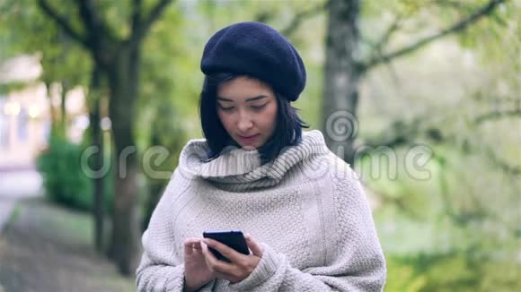迷人的亚洲女人在秋天公园里带着智能手机视频的预览图