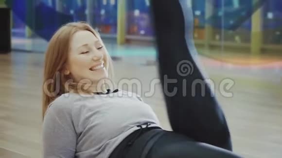 快乐的金发美女在健身房里躺着做劈叉视频的预览图