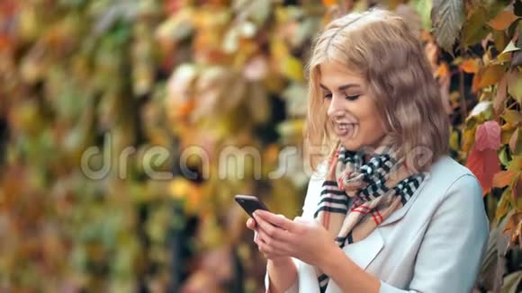 快乐美丽的女人微笑着在秋天公园用她的手机视频的预览图